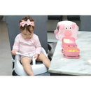 Toddler in a high chair, wearing a pink outfit and bow, next to pink food containers and a pig-themed bag.