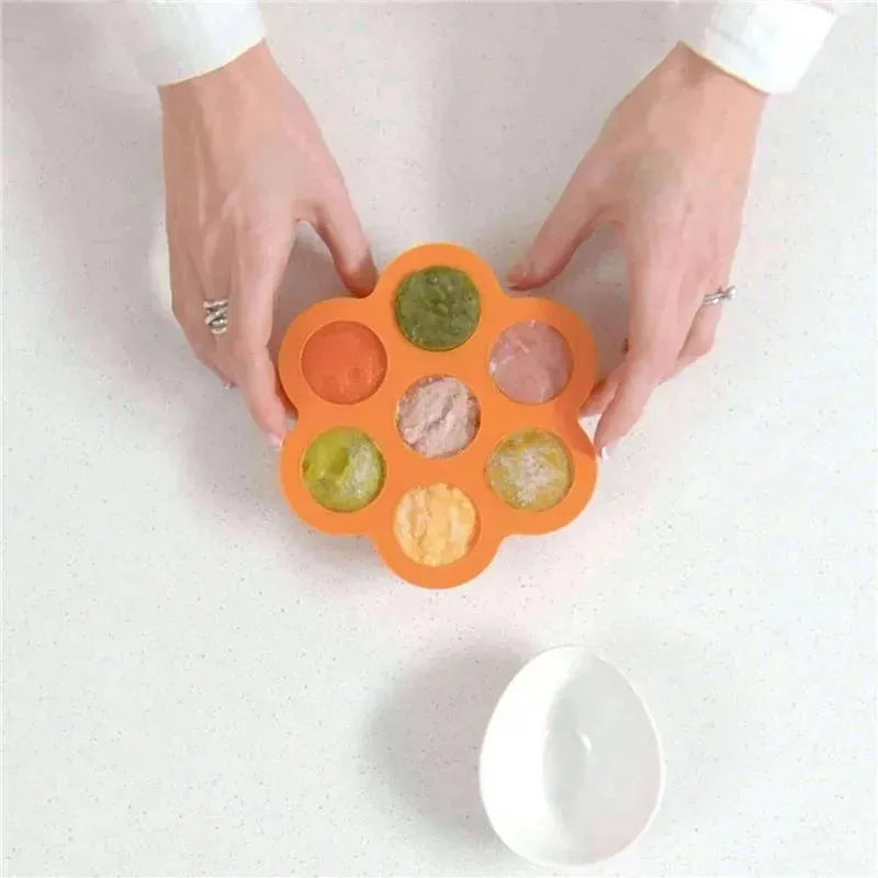Silicone baby food freezer tray with lid, featuring eight compartments filled with various pureed foods.