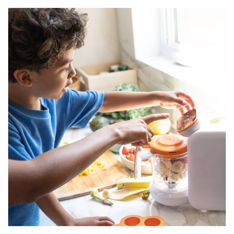 A child uses the Quark Quook 5-In-1 Baby Food Processor, preparing fruits and vegetables at a kitchen counter.