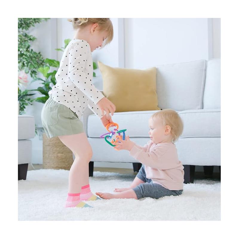 A young girl plays with a colorful Quark Thiingy teething toy while sitting on a rug next to a baby.