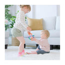 A young girl plays with a colorful Quark Thiingy teething toy while sitting on a rug next to a baby.
