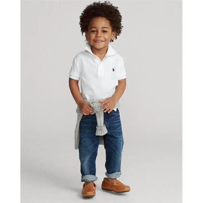Ralph Lauren Baby white performance jersey polo shirt on a young boy, paired with blue jeans and brown shoes, smiling confidently.