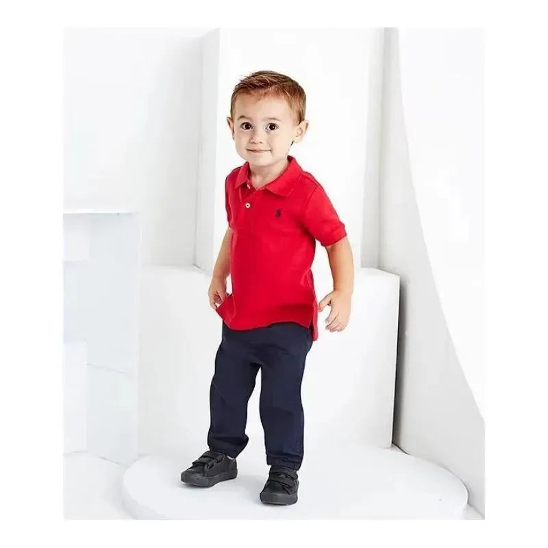 Red polo shirt on a young boy standing on a pedestal, wearing dark pants and black shoes, smiling at the camera.
