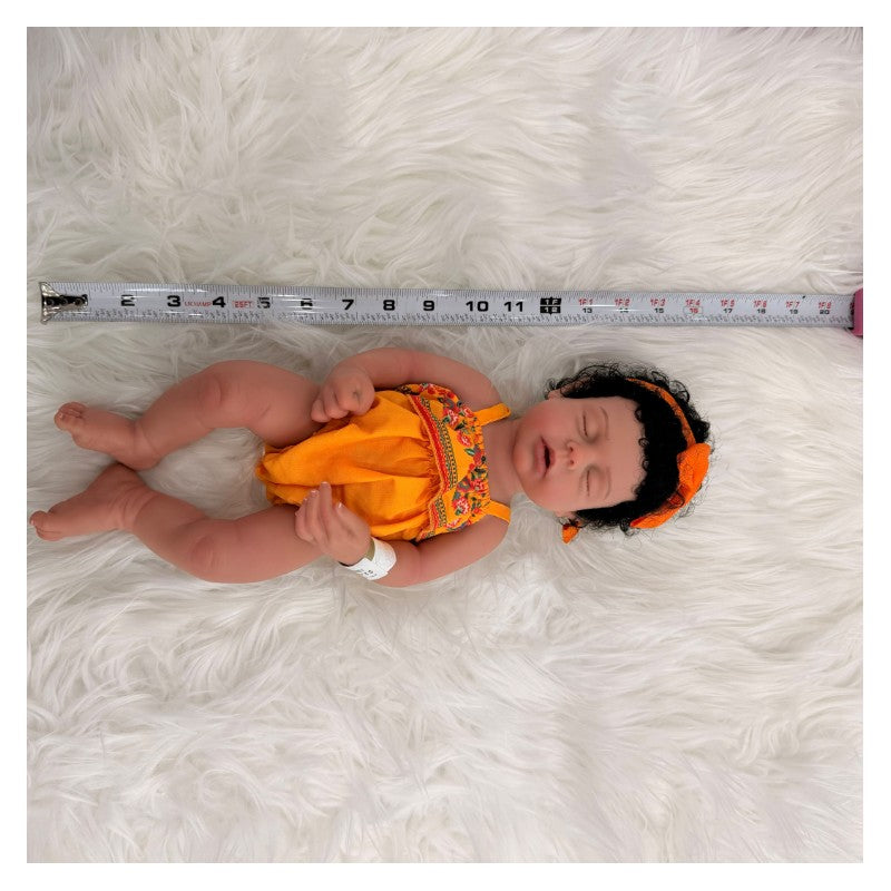 Reborn Baby Doll Arianna dressed in an orange outfit with a matching headband, lying on soft white fur with a tape measure beside her.