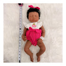 Reborn baby doll Emily, an African American full silicone doll with closed eyes, dressed in a white and pink outfit.