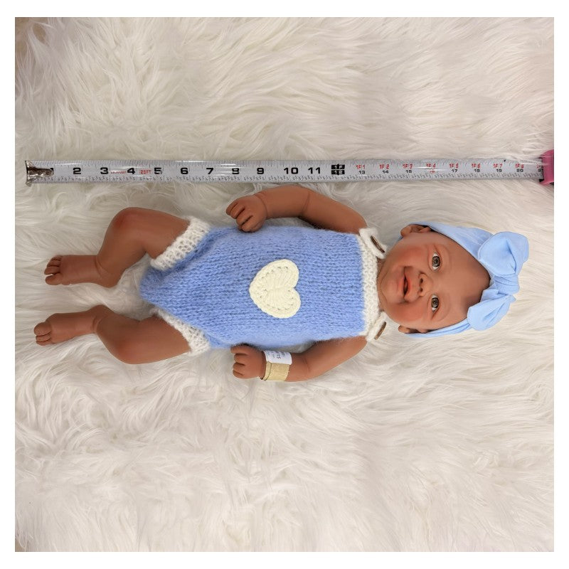 Bald African American reborn baby doll dressed in a blue knitted outfit with a heart, wearing a light blue headband.