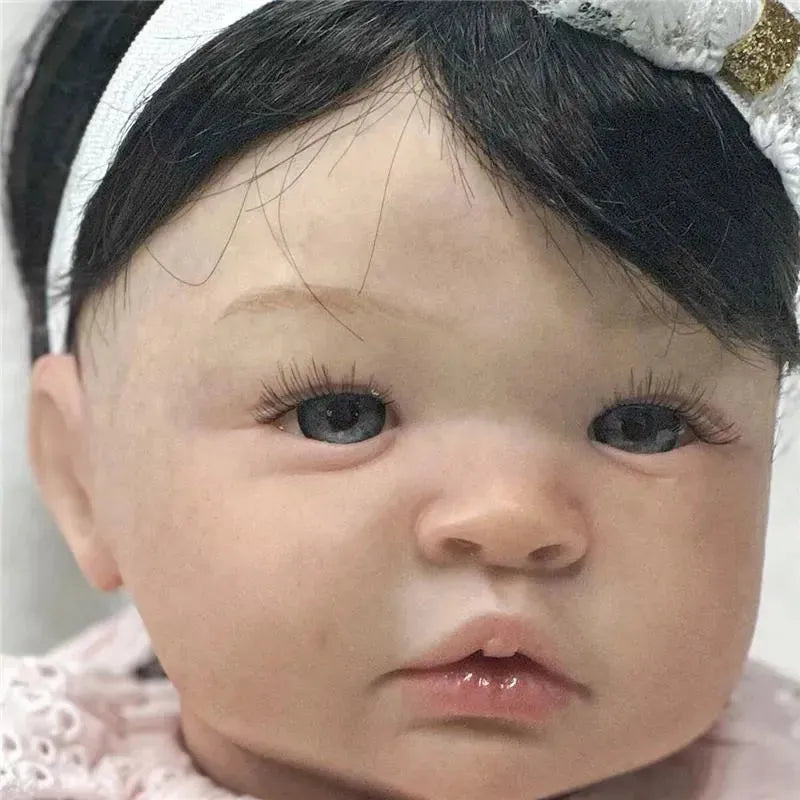Reborn baby doll named Shyann with white vinyl skin and black wig, featuring realistic details like blue eyes and eyelashes.