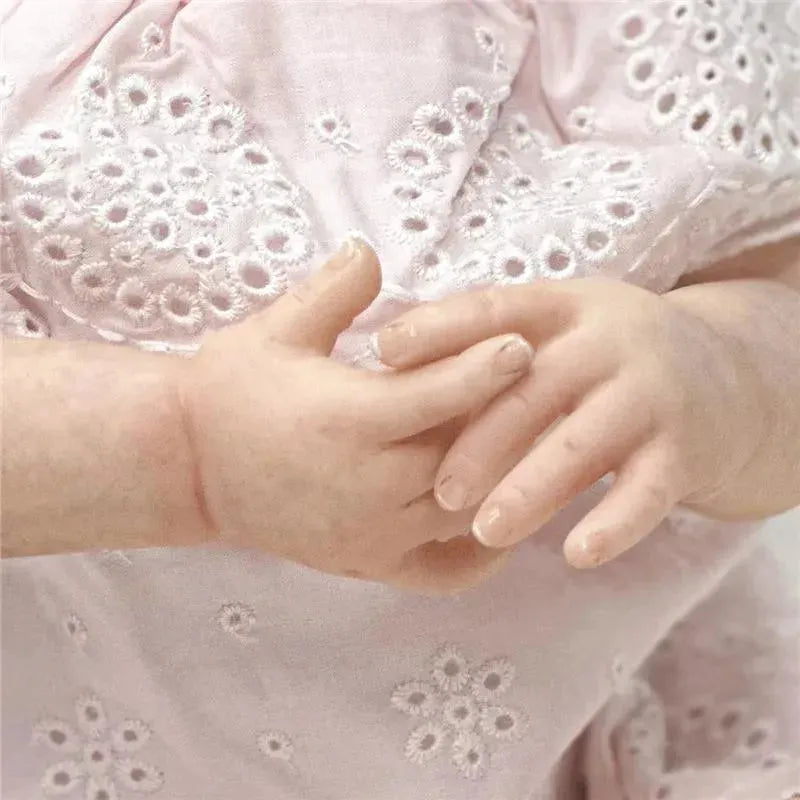 Reborn baby doll, Shyann, with realistic white vinyl skin and delicate hands, dressed in a pink embroidered outfit.