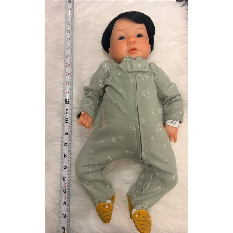 Reborn baby doll named Shyann, featuring white vinyl skin, black wig, wearing a green onesie with heart patterns and brown booties.