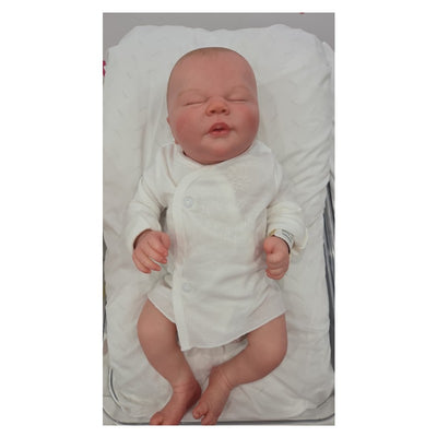 Reborn Doll White Vinyl Ever dressed in a white outfit, lying on a padded surface with a serene expression.
