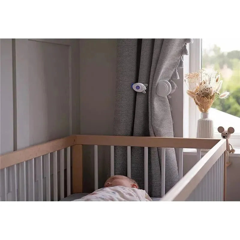 Portable sound-soother Rockit attached to curtains near a sleeping baby in a crib, creating a calming environment.