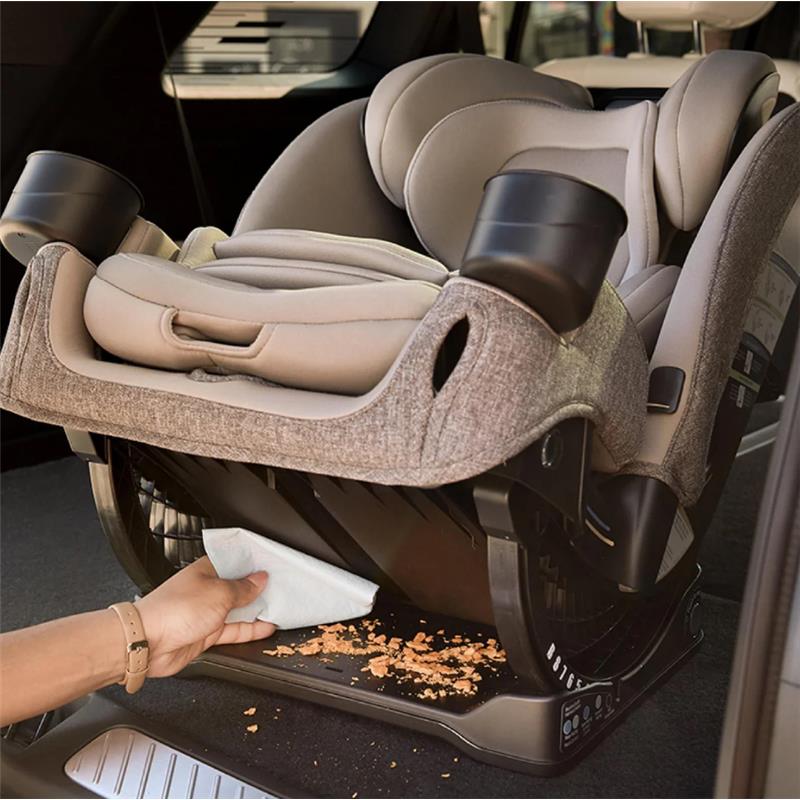 Romer Nexa All-in-One Convertible Car Seat in Truffle, with a hand cleaning crumbs from the base in a vehicle.