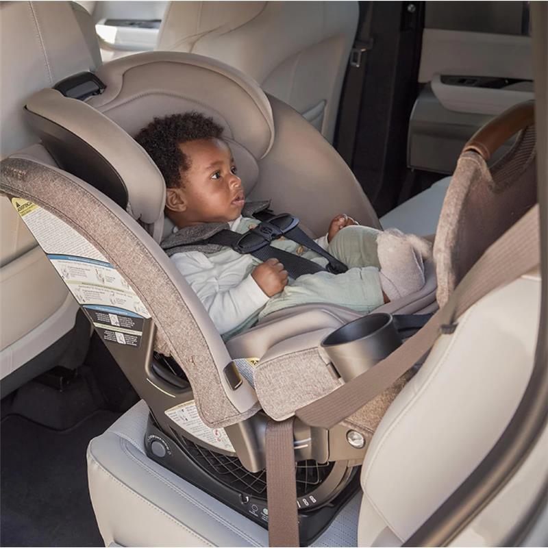 Child securely seated in a Romer Nexa All-in-One Convertible Car Seat, Truffle color, inside a vehicle.