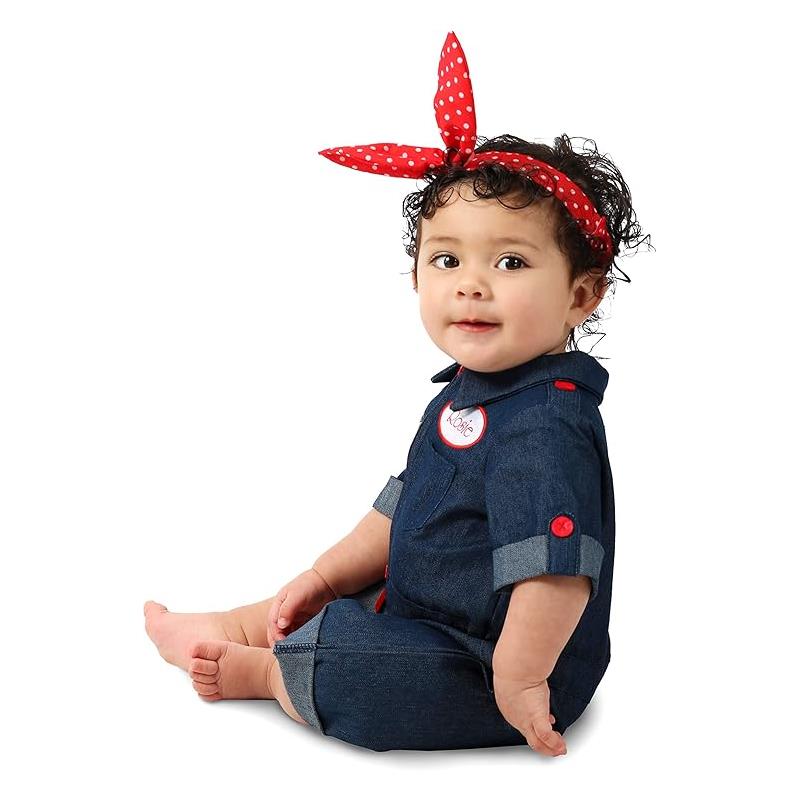 Baby wearing a denim Rosie the Riveter costume with a red polka dot headband, sitting and smiling.