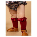 Dark cherry knee-high socks with lace ruffles and bows, worn by a toddler, paired with brown leather shoes.