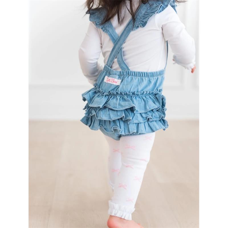Light wash flutter overall romper for baby girl with ruffled skirt, worn over white leggings with pink bows.