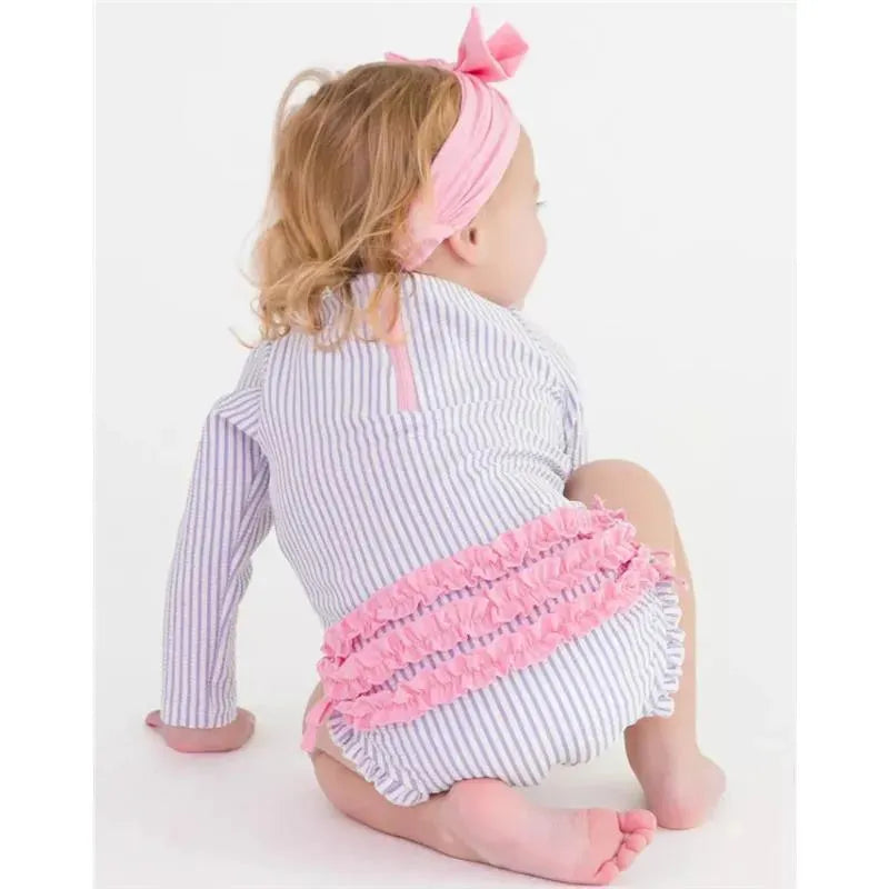 Baby girl wearing a lavender and white striped long sleeve rash guard with pink ruffles at the back.