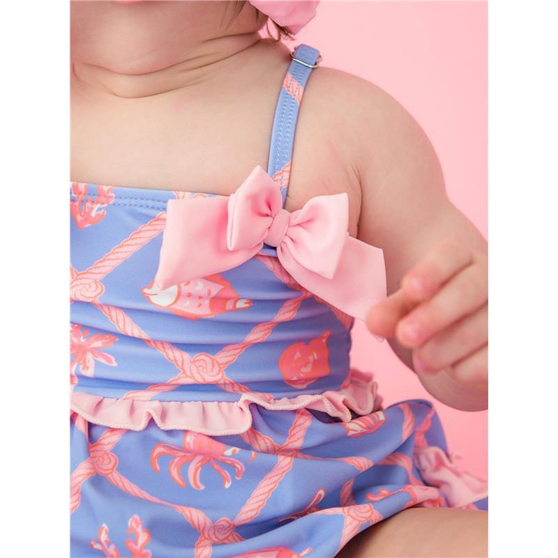 Baby girl in a tropical-themed one-piece swimsuit featuring a pink bow and ruffled trim, surrounded by seashell and crab prints.