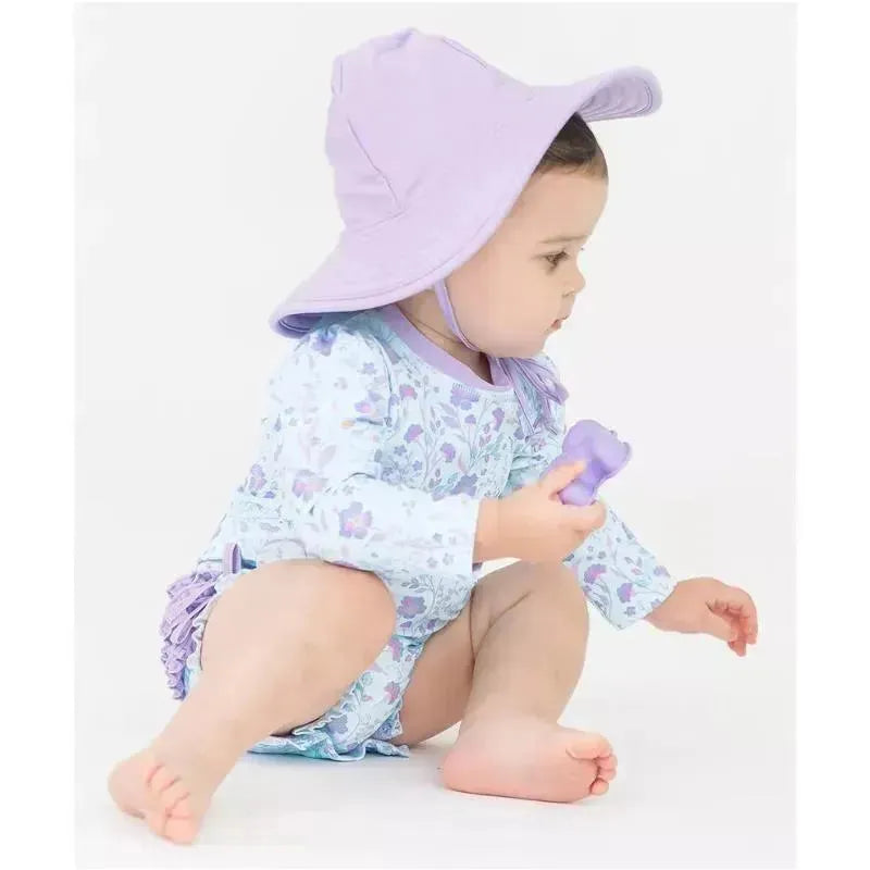 Toddler wearing a floral long sleeve rash guard and a purple sun hat, holding a small toy.