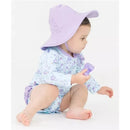 Toddler wearing a floral long sleeve rash guard and a purple sun hat, holding a small toy.