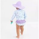 Toddler wearing a floral ruffle one-piece rash guard with long sleeves and a purple sun hat, holding a toy.