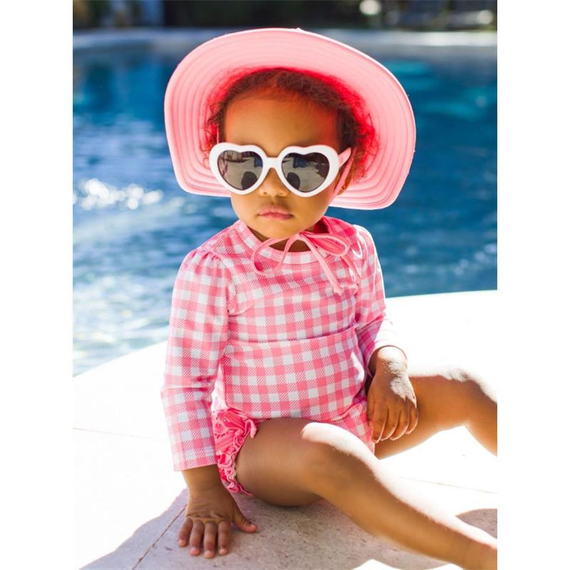Long sleeve one-piece rash guard in bubblegum pink worn by a child, paired with a pink sun hat and heart-shaped sunglasses.