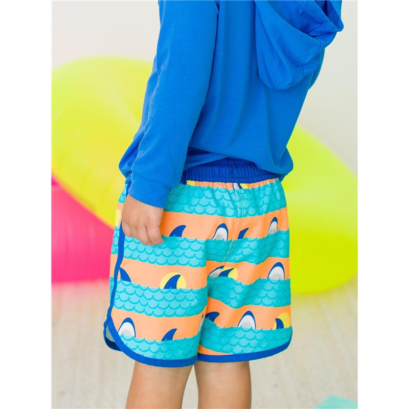 Boys swim trunks featuring a dolphin hem design in vibrant orange and blue with shark fins, paired with a blue long-sleeve shirt.