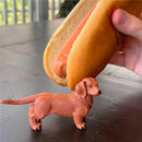 Dachshund figurine in orange 3.75 inches tall, positioned near a hand holding a hot dog bun with sausage.