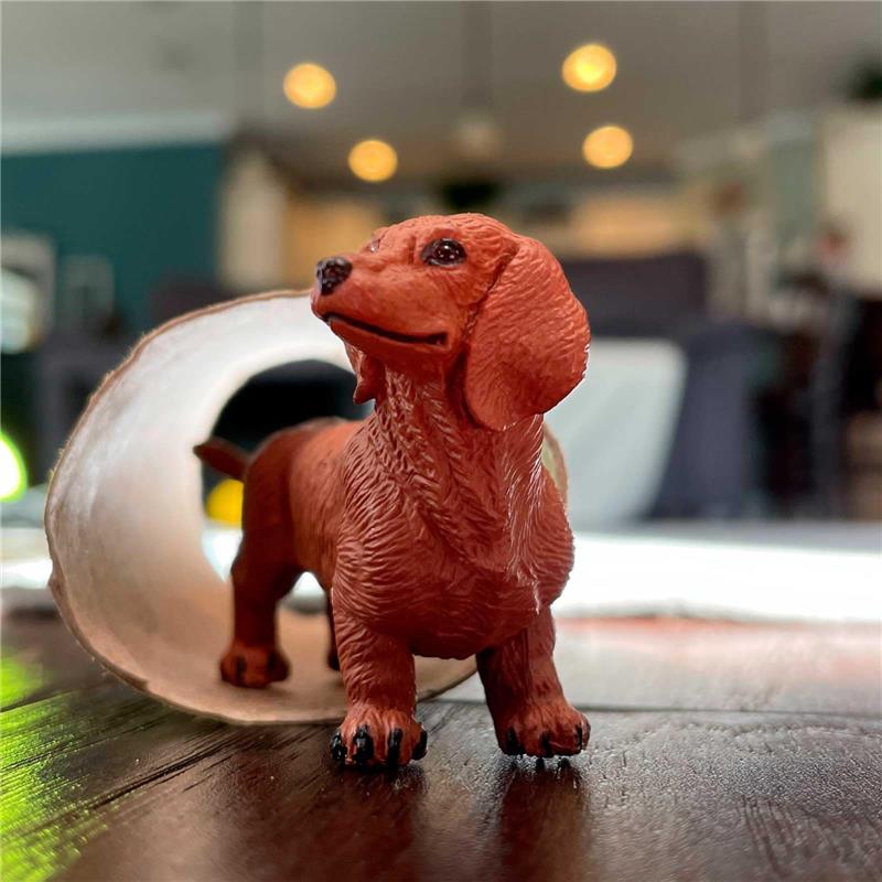 Dachshund figurine in brown plastic, standing on a wooden surface, with a visible tunnel in the background.