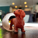 Dachshund figurine in brown plastic, standing on a wooden surface, with a visible tunnel in the background.