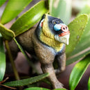 Mandrill figurine by Safari Ltd., featuring detailed colors and textures, set among green leaves.