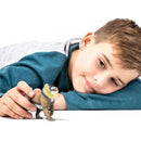 A boy lies on the ground, reaching for a realistic mandrill toy figure.