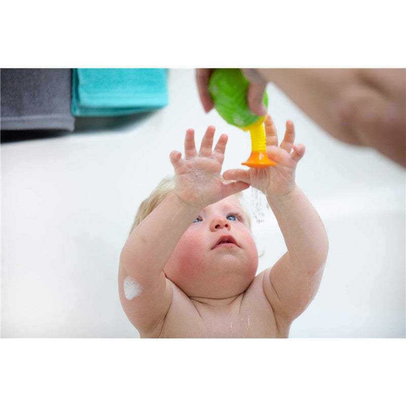 A baby reaching for a colorful bath toy being held by an adult, surrounded by bath supplies.