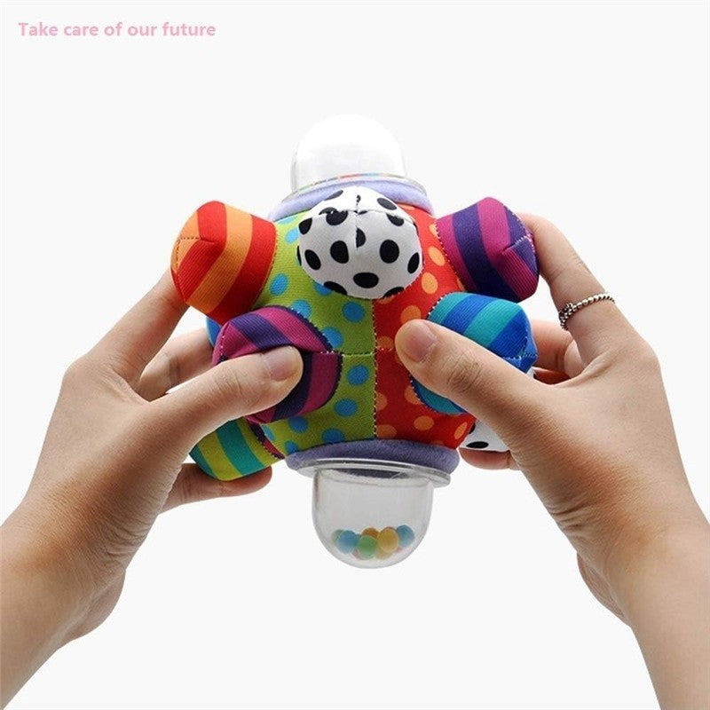 Colorful, textured developmental ball with a smiling face held by two hands, featuring small beads inside a clear bottom.