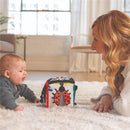 A baby and a woman engage on a soft rug, focused on a colorful Sassy Wimmer Discovery Cube featuring a ladybug design.