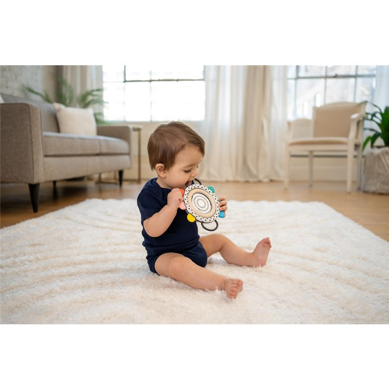 Baby sitting on a soft rug, holding a Sassy Wimmer Grasp & See Mirror with colorful attachments, exploring its features.
