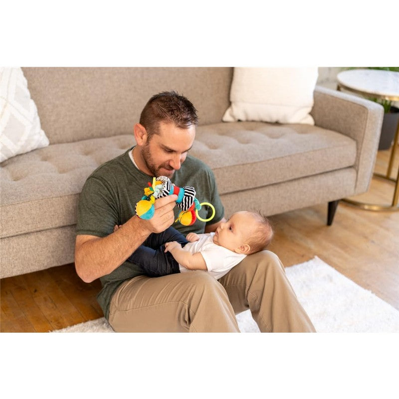 A man plays with a colorful Sassy Wimmer Zaggles toy, engaging with a baby seated in front of him.