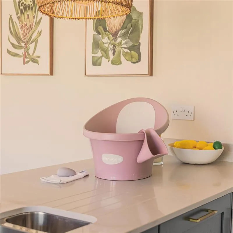 Shnuggle Bath Rinse Jug in Blossom color displayed on a countertop with a bowl of lemons and art on the walls.