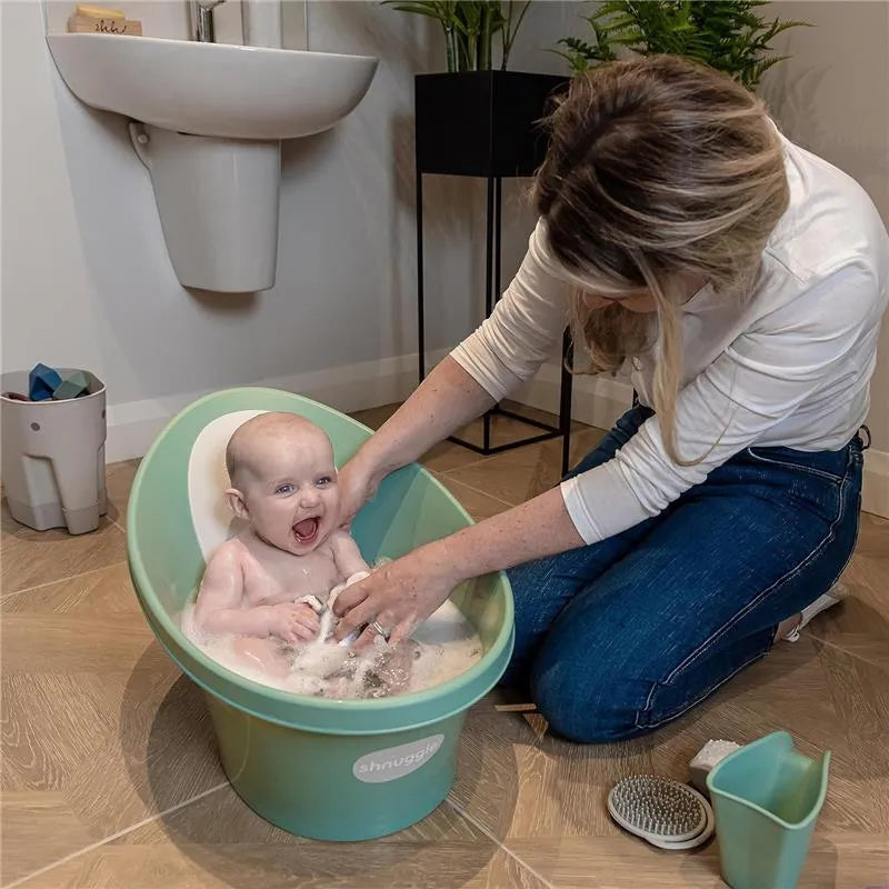 A baby enjoys bath time in a Shnuggle bath rinser jug while being gently washed by an adult.