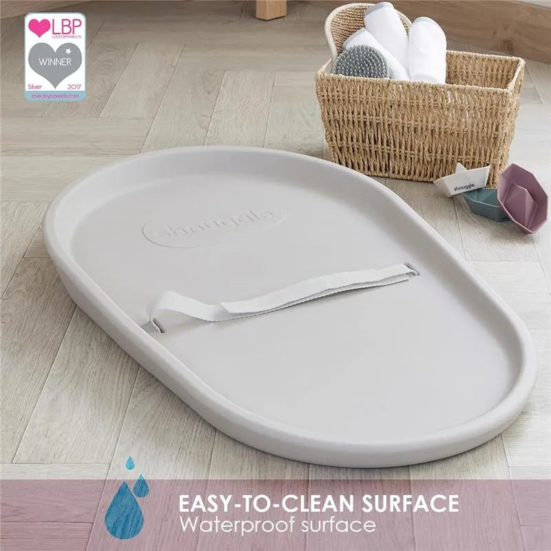 Squishy grey baby changing diaper pad by Shnuggle with an easy-to-clean waterproof surface displayed on light wood flooring.