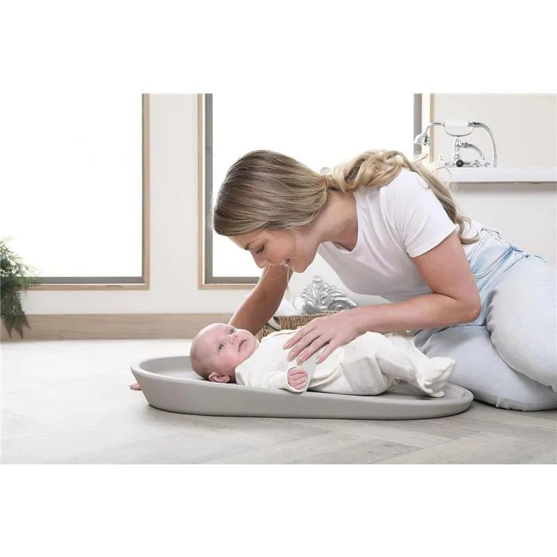Mother gently interacts with a baby on a taupe Shnuggle changing pad in a bright, modern room.