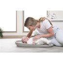 Mother gently interacts with a baby on a taupe Shnuggle changing pad in a bright, modern room.