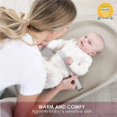 Squishy taupe baby changing diaper pad with a smiling baby wearing a cream outfit, and a woman gently interacting with the baby.
