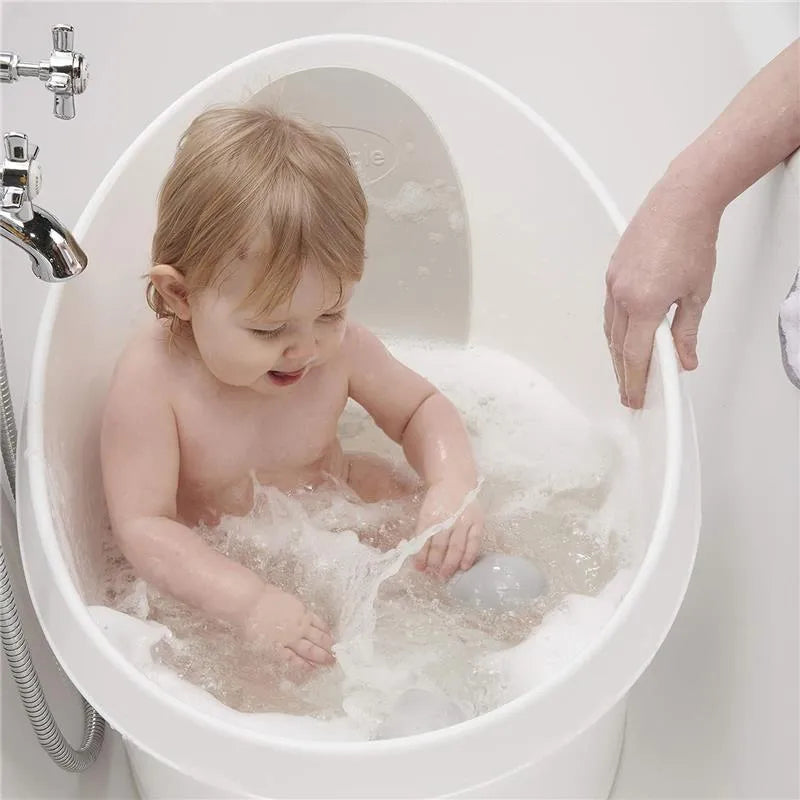 Toddler enjoying a bath in the Shnuggle white and grey bath tub, splashing water with soft bath toys.