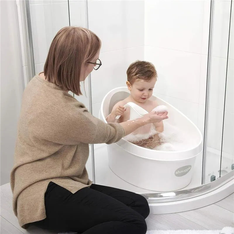 Toddler bath tub in white and grey with a child playing in bubbles, while a caregiver assists beside.