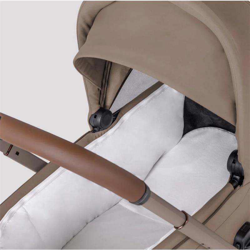 Modular stroller and bassinet in Champagne color with a padded interior and sturdy brown handle.