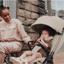 Lightweight Silver Cross Clic stroller in Latte color with a child sitting comfortably, smiling and holding their hands to their mouth.