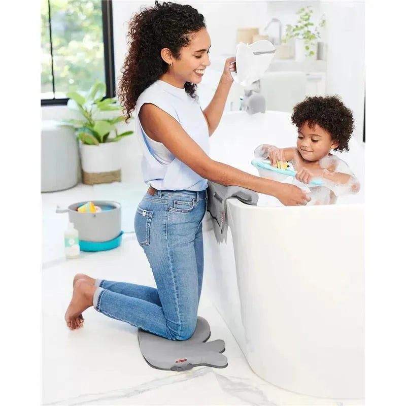 A woman kneels on a gray bath mat, smiling while rinsing a child in a white bathtub with the Skip Hop Moby Waterfall Bath Rinser.