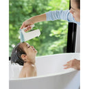 A child in a bathtub smiles as a caregiver pours water from a Skip Hop Baby Bath Rinse Cup over their head.