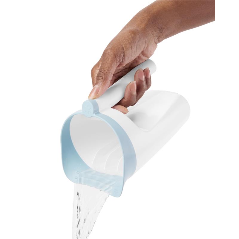 Hand holding a white Skip Hop baby bath rinse cup with a blue rim, pouring water smoothly for bath time use.